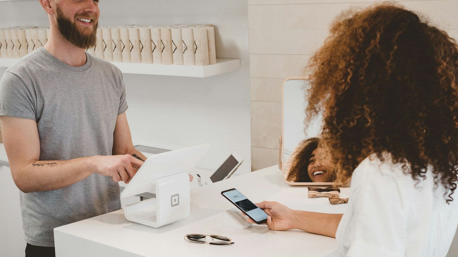 A customer paying with a phone at a shop counter while the assistant watches.